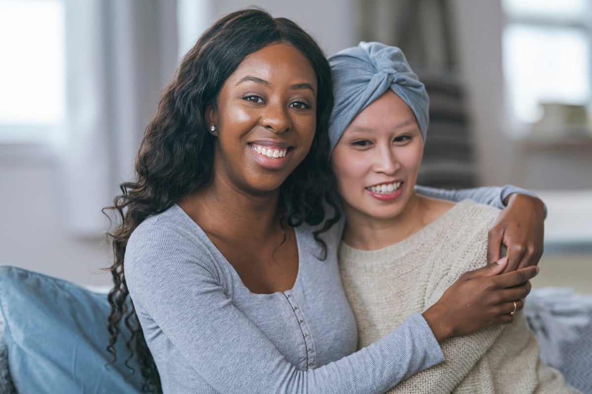 Smiling black woman embracing Asian friend with cancer