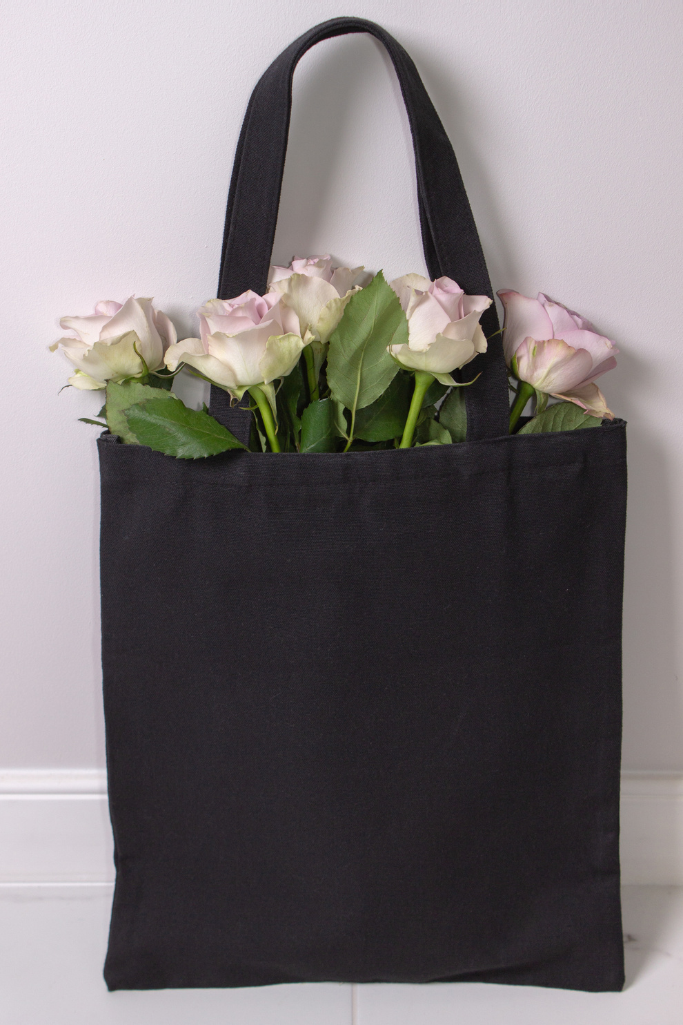 Black cotton tote bag with light violet roses inside. Styled photography